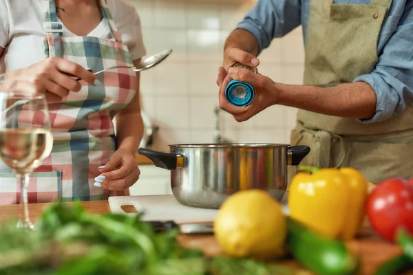 Bir kadının elinde kaşıkla çorbaya baharat ve biber eklerken çekilmiş bir fotoğraf. Çift mutfakta birlikte yemek hazırlıyor. Evde yemek, İtalyan mutfağı.