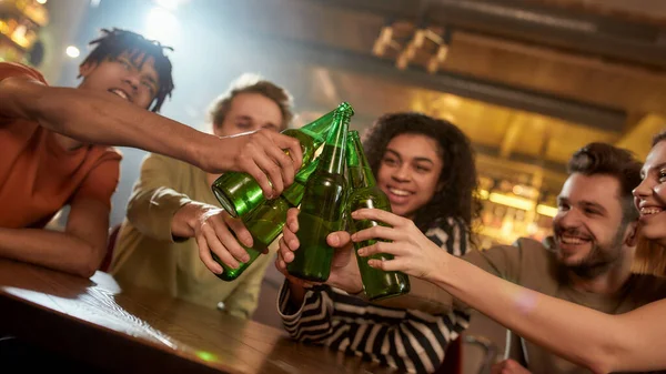 Un grupo de amigos felices en el bar viendo partidos deportivos en la televisión juntos, bebiendo cerveza, tintineando botellas y animando al equipo. Gente, ocio, amistad y entretenimiento — Foto de Stock