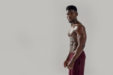 Formda hissediyorum. Genç kaslı Afro-Amerikan erkek çıplak gövdesiyle kameraya bakarken gri arka planda çıplak poz veriyor. Spor, spor, vücut geliştirme konsepti