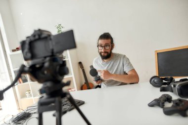 Erkek teknoloji blogcusu beklemede, kulaklıklara işaret ederek video blogu veya video blogu kaydederken ev stüdyolarındaki yeni cihazlar hakkında