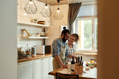 Aşık genç bir çift evde sebzeli pizza yapmak için hamur hazırlıyor. Kadın ve erkek önlük giyiyor, evde birlikte yemek pişiriyorlar. Hobi, yaşam tarzı