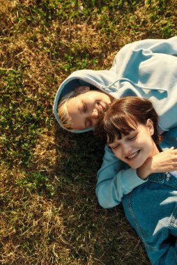 Mutlu lezbiyen kızlar yaz parkında çimlerin üzerinde yatıyor, aşıklar gülüyor, birlikte dışarıda vakit geçiriyorlar.