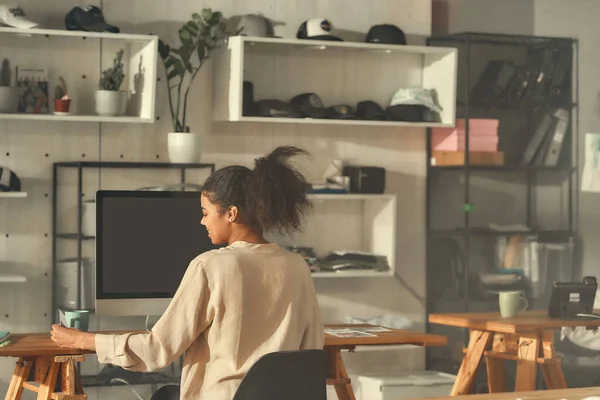 Custom graphic design. Portrait of female worker looking at notes while drawing sketches logo design using pc. Young woman working at custom T-shirt, clothing printing company