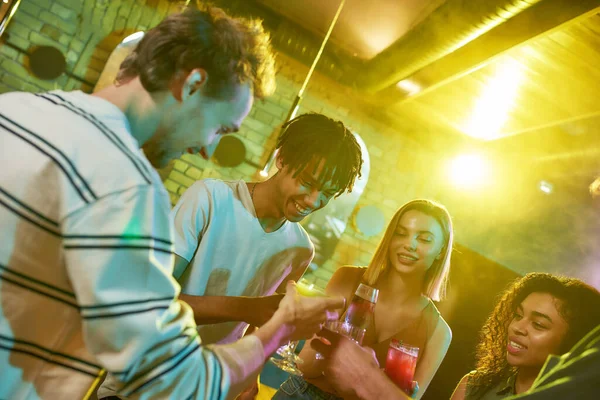 Träffa nya vänner. En grupp vänner, unga kvinnor och män skålar medan de har roligt, dricker cocktails, umgås på nattklubben — Stockfoto