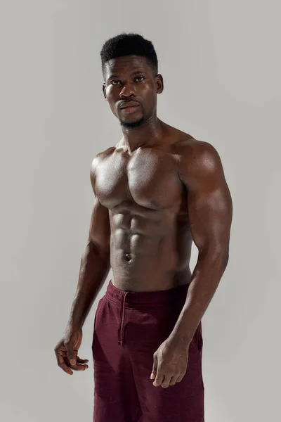 Corpo saudável. Homem americano africano muscular olhando para a câmera, mostrando seu tronco nu enquanto posava sem camisa isolado sobre fundo cinza. Esportes, treino, conceito de musculação — Fotografia de Stock