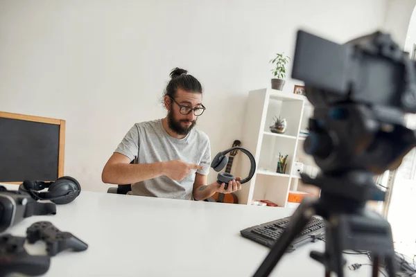 Hombre blogger tecnología celebración, apuntando a los auriculares durante la grabación de blog de vídeo o vlog sobre nuevos aparatos en el estudio en casa —  Fotos de Stock