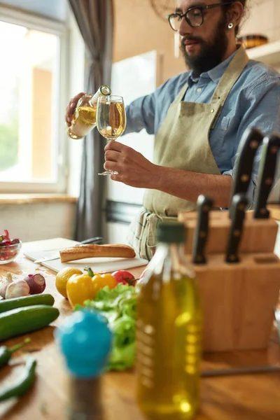 Νεαρός, Ιταλός μάγειρας ρίχνει λευκό κρασί στο ποτήρι ενώ ετοιμάζει γεύμα στην κουζίνα. — Φωτογραφία Αρχείου