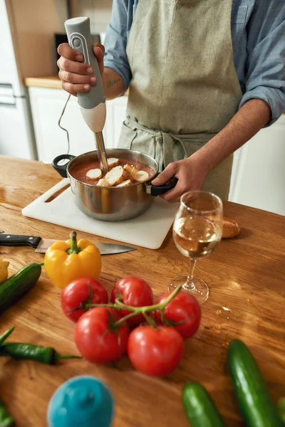 Καλλιεργημένη βολή του ανθρώπου, σεφ μάγειρας χρησιμοποιώντας το χέρι μπλέντερ, ανάμειξη ψιλοκομμένα λαχανικά και ψωμί, ενώ την προετοιμασία ιταλικό γεύμα στην κουζίνα — Φωτογραφία Αρχείου