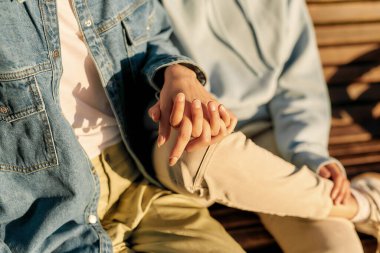 Lezbiyen bir çiftin ellerini kapatıyoruz. Güneşli bir günde iki kız el ele tutuşuyor. Birlikte dışarıda vakit geçiriyorlar.