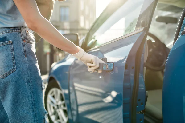 Close-up van de hand van de vrouw in beschermende handschoen openen van de blauwe auto deur, Beschermende maatregelen tegen bacteriën, virussen, coronavirus pandemie — Stockfoto