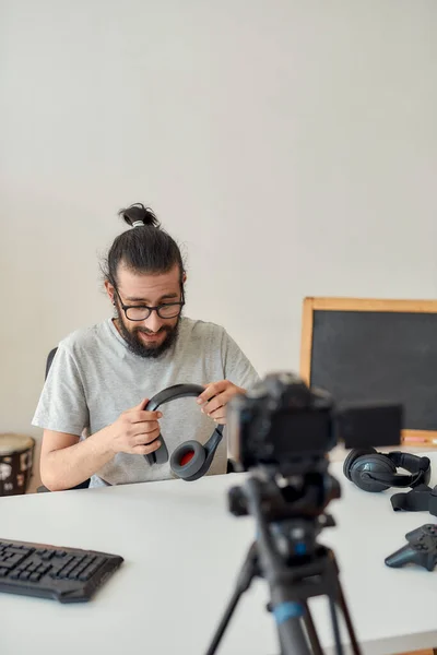 Man teknik bloggare i glasögon håller och visar hörlurar medan du spelar in video blogg eller vlog om nya prylar hemma studio — Stockfoto