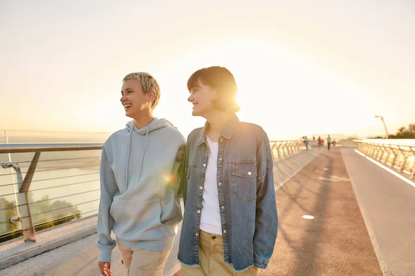 Voel de liefde. Gelukkig lesbisch stel dat opzij kijkt, lachend over de brug loopt en samen naar de zonsopgang kijkt. Homoseksualiteit, LGBT en liefdesconcept — Stockfoto