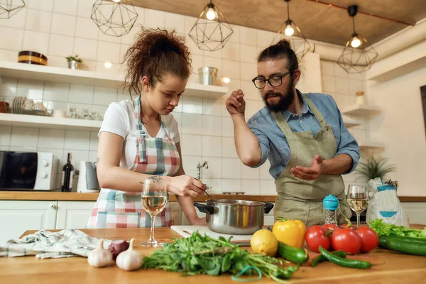 Італієць додає перець, Спайс до супу, а жінка перемішує його ложкою. Пара готує вечерю разом на кухні. Куховарство вдома, італійська кухня. — стокове фото