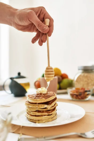 Hand holding dipper, adding honey on top of stack of sweet tasty pancakes — Stock Photo, Image