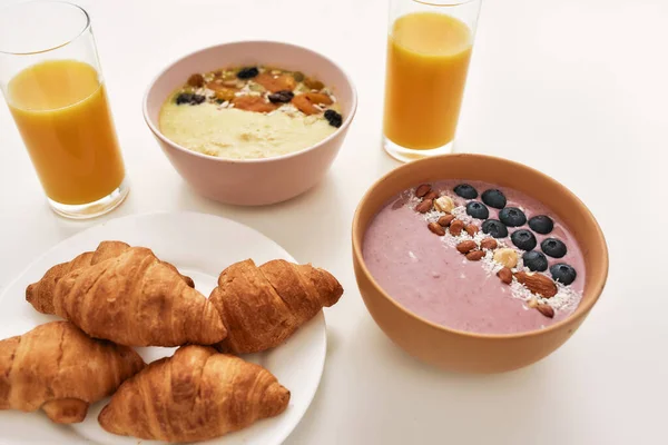 Close up of smoothie bowl with fresh berries, orange juice in glass and croissants on a plate isolated over white background — Stock Photo, Image