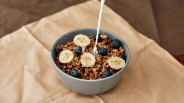 Ev yapımı granola 'ya fındıklı, balı, yaban mersinli ve muzlu bir tabakta süt eklenerek peçeteyle servis ediliyor.