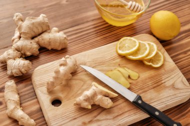 Soğuk algınlığı ve grip ilacına hazırlık içeceği, tahtayı kapat, bıçak, taze zencefil, limon, bal, ahşap masa üzerinde dipper olan bir kasede.