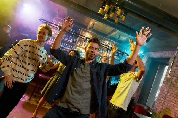 Live your weekend. Handsome caucasian young man enjoying evening, celebrating, dancing at party in the bar. People having fun in the background — Stock Photo, Image