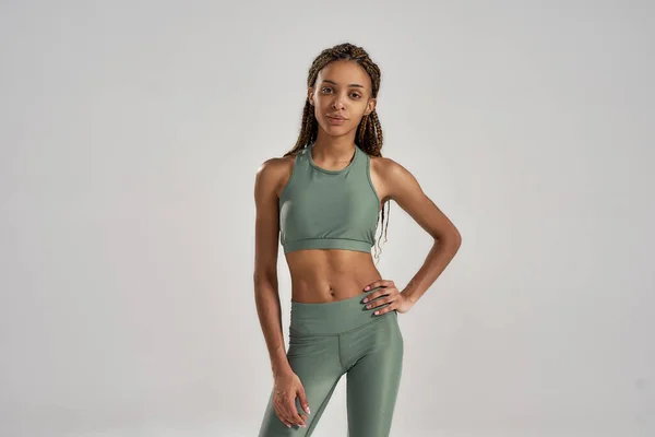 Estilo de vida activo y saludable. Joven atlética delgada mujer de raza mixta en ropa deportiva mirando a la cámara mientras posa aislado sobre fondo gris — Foto de Stock