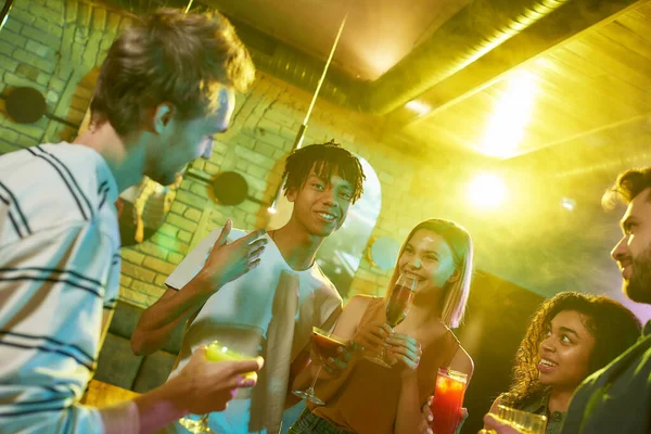 Festa hela natten. En grupp vänner, unga kvinnor och män chattar medan de har roligt, dricker cocktails, umgås på nattklubben — Stockfoto