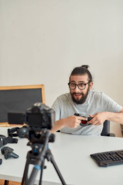 Gözlüklü bir erkek teknoloji blogcusu video blogu veya video blogu kaydederken heyecanlı görünüyor, kulaklıkları tutuyor ve gösteriyor.