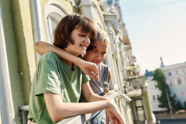 Portret van een jong meisje dat naar beneden kijkt, glimlachend terwijl ze op het balkon staat met haar vriendin. lesbisch paar spenderen hun dag samen — Stockfoto
