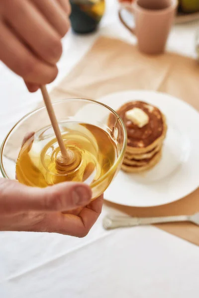 Close up of hands holding a bowl with honey, A stack of sweet tasty pancakes on the table, Process of preparing breakfast — Stock Photo, Image