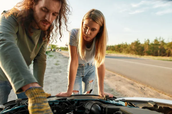 Meisje heeft problemen met haar auto, Man kijkt onder de motorkap van gebroken auto, terwijl het helpen van jonge vrouw om het probleem op te lossen — Stockfoto