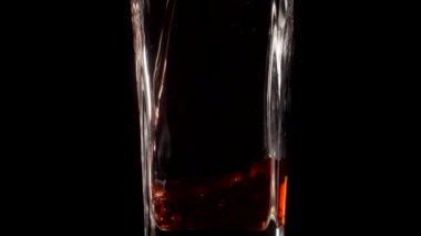 Şeffaf bir bardağa siyah zemin üzerine nar suyu dökerken süper yavaş çekim. Kapatın. Sağlıklı içecek, vitaminler, meyve konsepti
