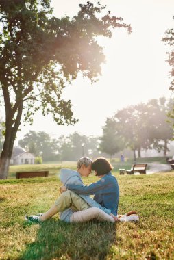 Yaz parkında çimlerin üzerinde oturan mutlu lezbiyen çift. Aşık kadınlar birlikte zaman geçirir, birbirlerine sarılırlar.