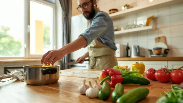 Genç adam, İtalyan aşçı sebze doğruyor ve sağlıklı yemek hazırlarken tencereye koyuyor, mutfakta çorba yapıyor. İtalyan mutfağı kavramı