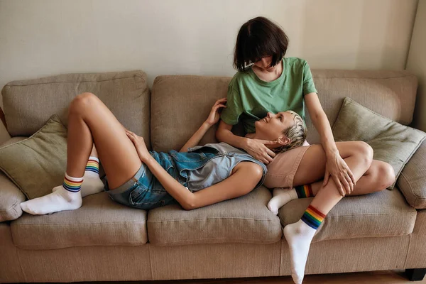 Гомосексуальна пара лесбійок дивиться один на одного, розслабляючись разом на дивані вдома — стокове фото