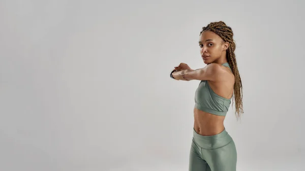 Giovane donna fitness razza mista in abbigliamento sportivo esercizio mentre in piedi isolato su sfondo grigio — Foto Stock