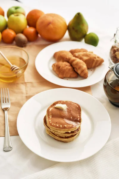 Close up of sweet tasty pancakes, croissants, honey in a bowl and various fruits, Breakfast served on the table — Stock Photo, Image