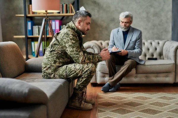Healing process. Full length shot of middle aged military man looking away during therapy session with psychologist. Soldier suffering from depression, psychological trauma. PTSD concept — Stock Photo, Image