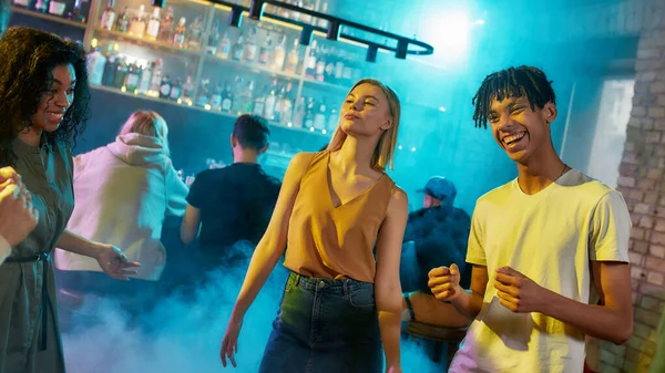 Atractiva mujer joven caucásica y chico de raza mixta divirtiéndose, bailando con amigos en la fiesta en el bar — Foto de Stock