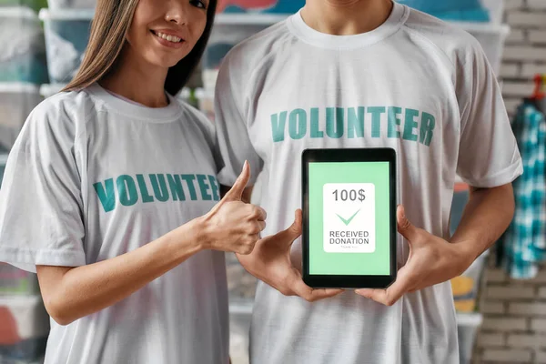 寄付のためのタブレットPC 、男の広告や推薦アプリを保持しながら慈善のために働く、親指を表示する若い多様なボランティアの作物のショット — ストック写真