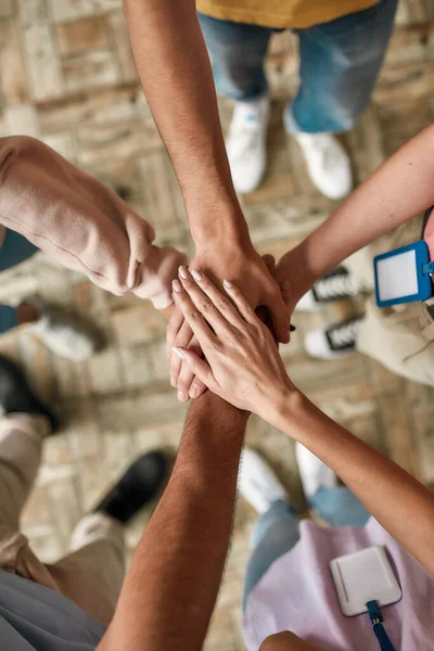 Vista superior de diversos jóvenes voluntarios poniendo sus manos encima de los demás como un equipo real, mientras que de pie en la oficina de la organización benéfica — Foto de Stock