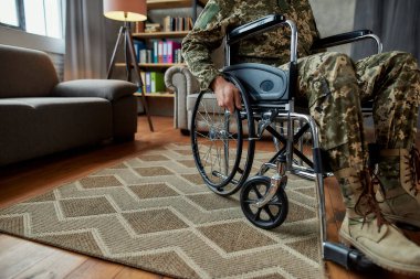 Engelli. Oturma odasında terapi sırasında tekerlekli sandalyede kamuflaj giyen engelli bir askerin görüntüsü. Travma Sonrası Stres
