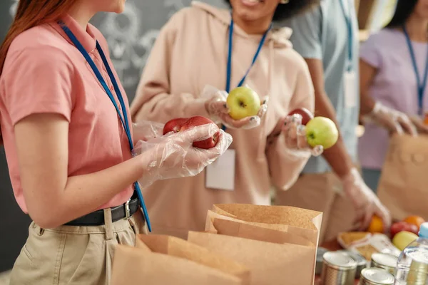 リンゴを手にした手袋をはめたボランティアの集団撮影、紙袋の中の貧しい人々のための食糧の分別、寄付プロジェクトに取り組むチーム — ストック写真