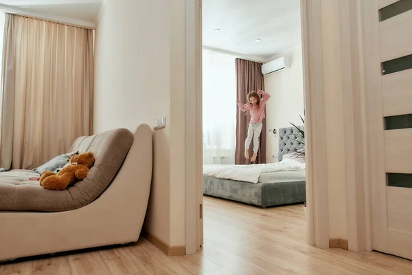 Small happy girl having a good time jumping barefoot on a huge bed in bright bedroom at home — Stock Photo, Image