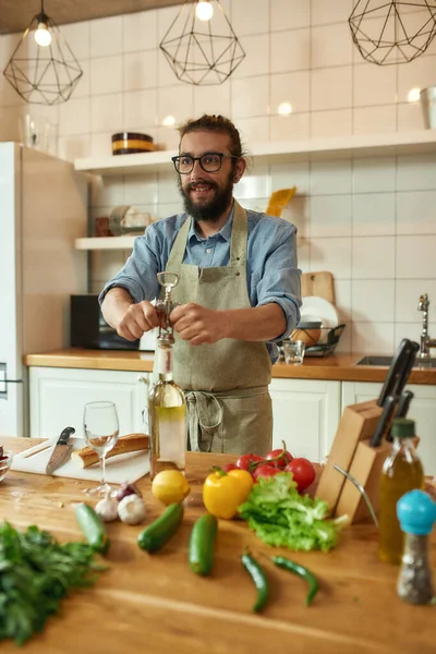 Молодий чоловік, італійський кухар, виглядає веселим, відкриваючи пляшку білого вина з штопор на кухні. — стокове фото
