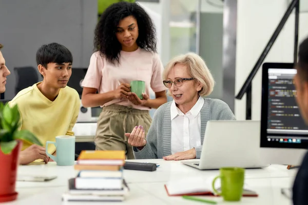 Aged woman, senior intern chatting with her young colleagues, Friendly workers talking with new employee during coffee break at work — Stock Photo, Image