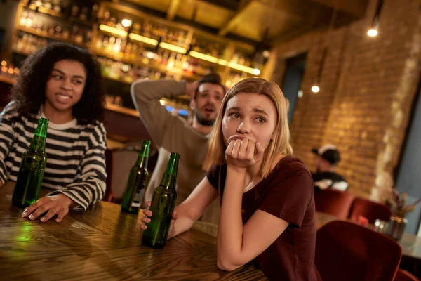 Friends looking disappointed while watching sports match on TV together, drinking beer and cheering for team in the bar. People, leisure, friendship and entertainment concept