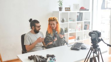 Bir erkek ve bir kadın, kulaklıkları tartışıyor. Genç erkek ve kadın teknoloji blogcusu evdeki yeni cihazlar hakkında video blogu veya video blogu kaydediyor