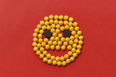 Gülümseme şeklinde uzanan sarı ve siyah hapların üst görüntüsü, kırmızı arkaplanda izole edilmiş bir yüz. Sağlık ve tedavi kavramı.