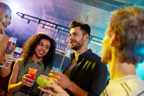 Recorte de grupo de amigos, adultos jóvenes, hombres y mujeres que se divierten mientras brindan, beber cócteles de pie en el club nocturno — Foto de Stock