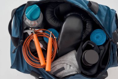 Spor çantasının yanına spor çantası ya da gri arka planda izole edilmiş eğitim ekipmanı koyun. Boks eldivenleri, el ambalajları, giysiler, bir şişe su ve atlama ipi.
