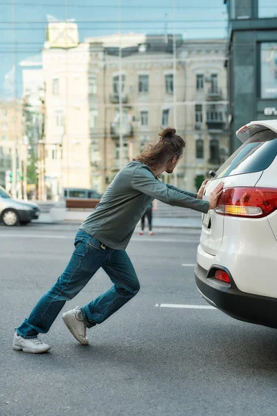 Volledige shot van de man in casual slijtage duwen een kapotte auto of een auto uit gas, staan op de weg — Stockfoto