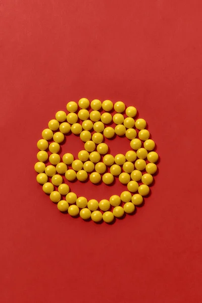 Horní pohled na žluté kulaté pilulky ležící ve tvaru úsměvu, tvář izolovanou přes červené pozadí. Koncepce zdravotní péče a léčby. — Stock fotografie